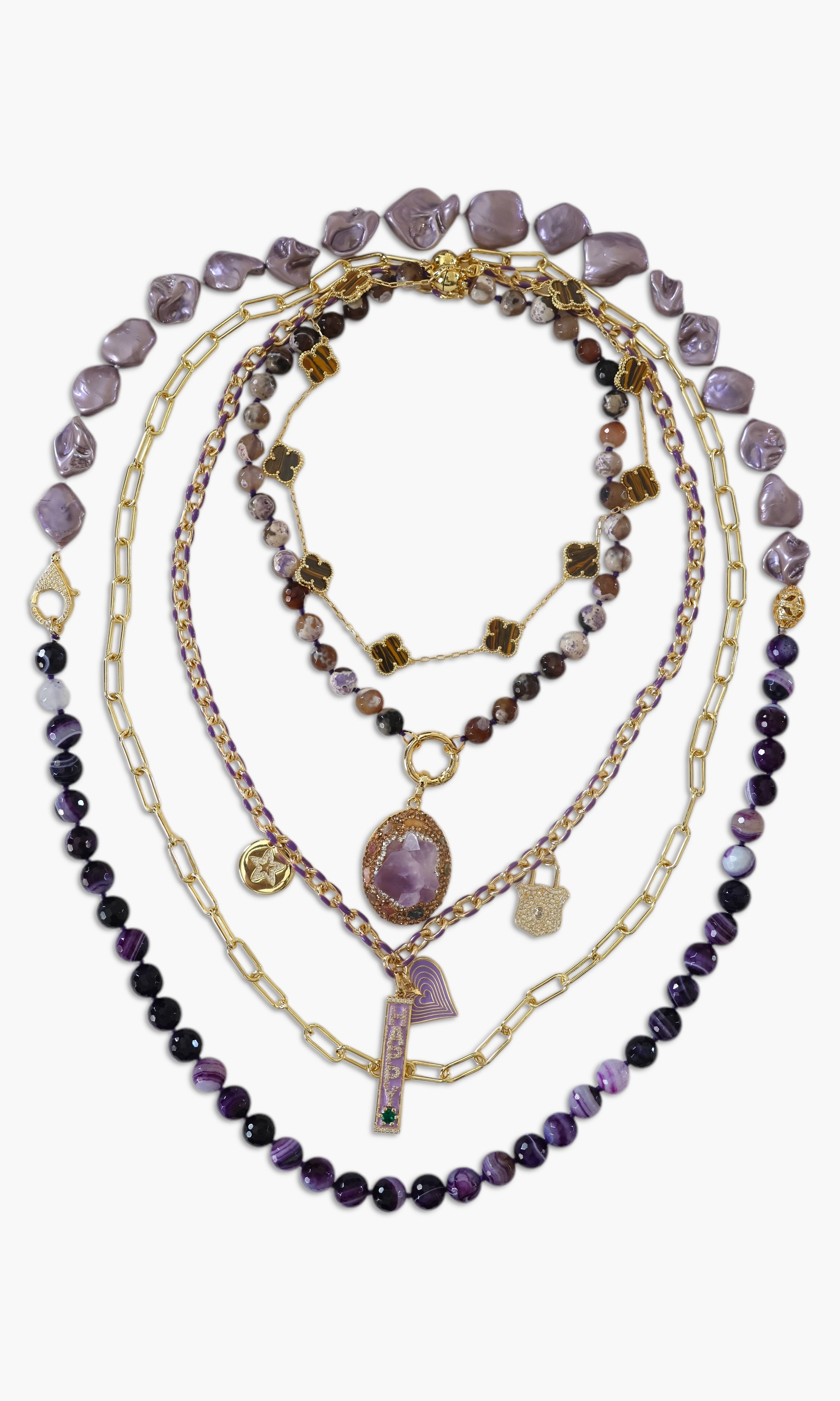 A person wearing multiple necklaces with amethyst stones and gold accents. The necklaces are part of a stack, and the person is holding some of the necklaces, showcasing the jewelry.