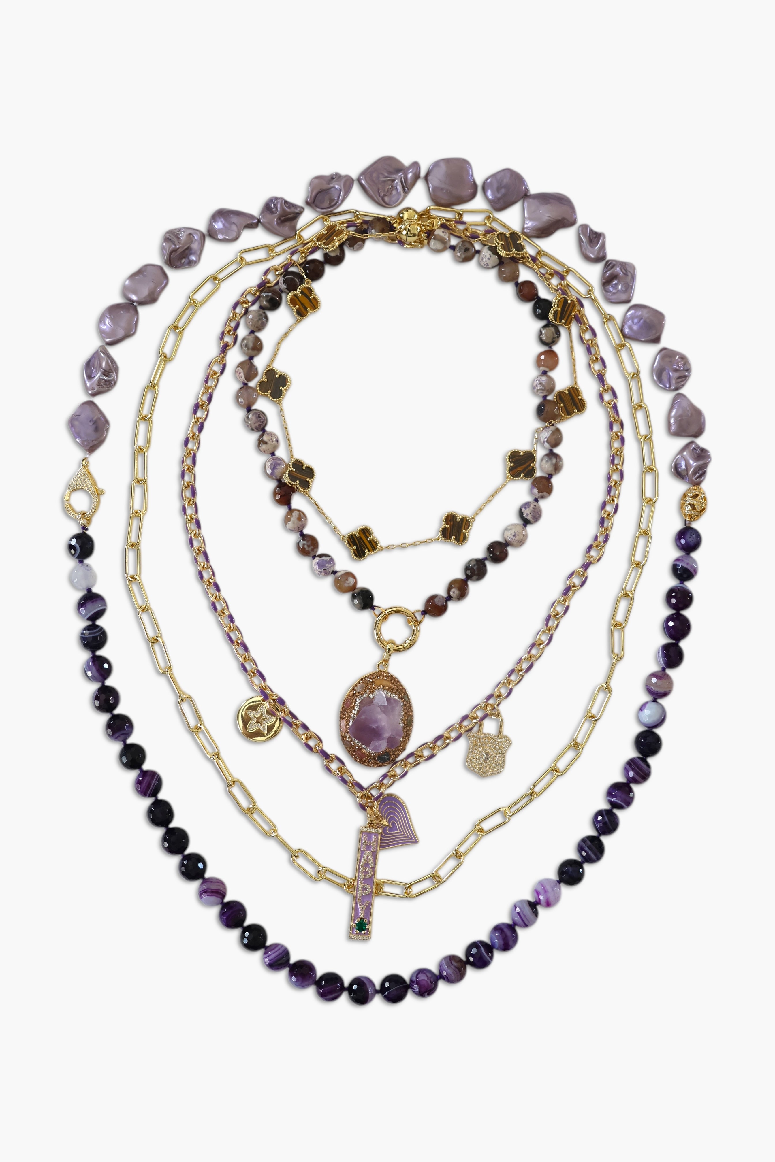 A person wearing multiple necklaces with amethyst stones and gold accents. The necklaces are part of a stack, and the person is holding some of the necklaces, showcasing the jewelry.