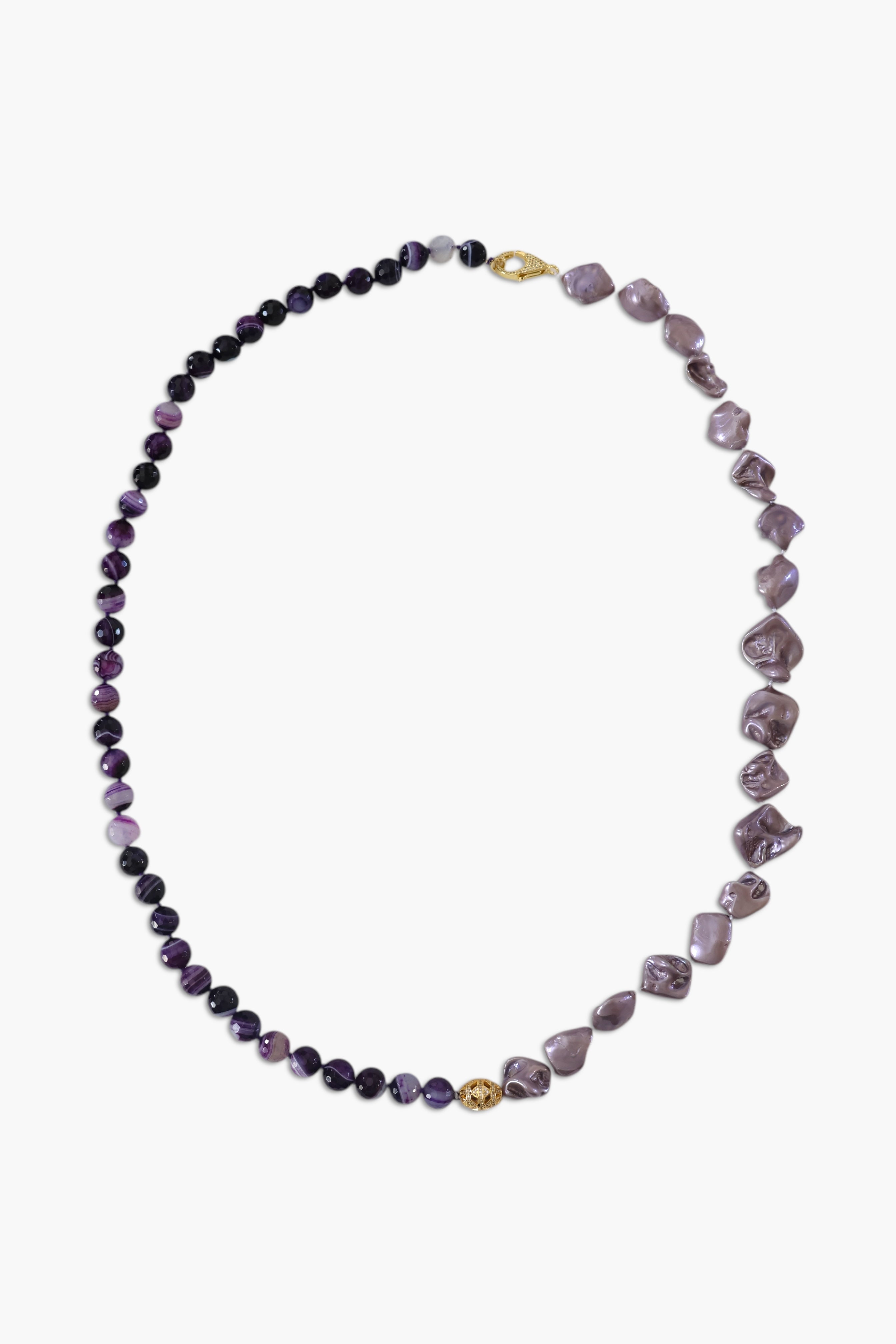 A person wearing multiple necklaces with amethyst stones and gold accents. The necklaces are part of a stack, and the person is holding some of the necklaces, showcasing the jewelry.