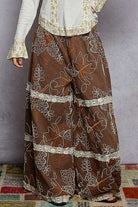 Brown patterned pants with white embroidery on a gray background