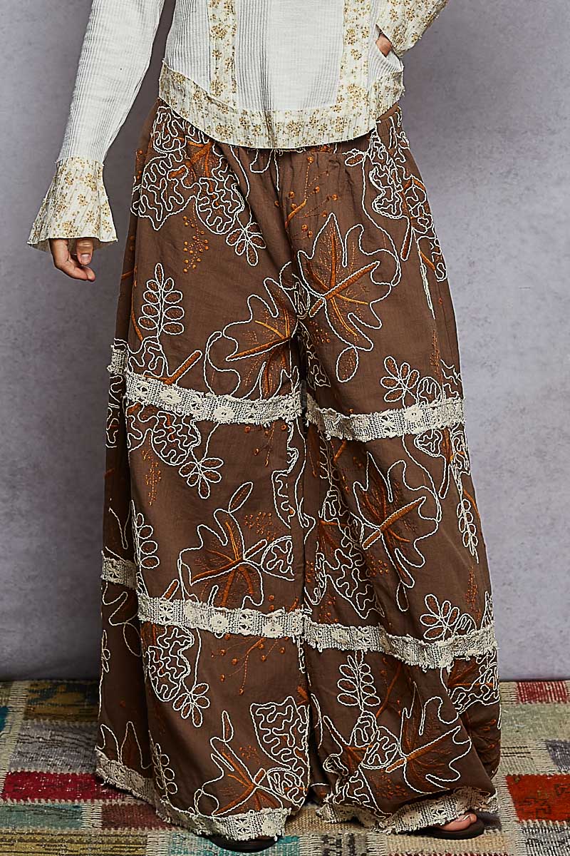 Brown patterned pants with white embroidery on a gray background