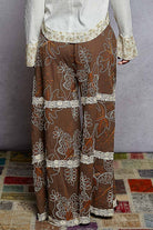 Brown pants with white floral embroidery on a patterned rug