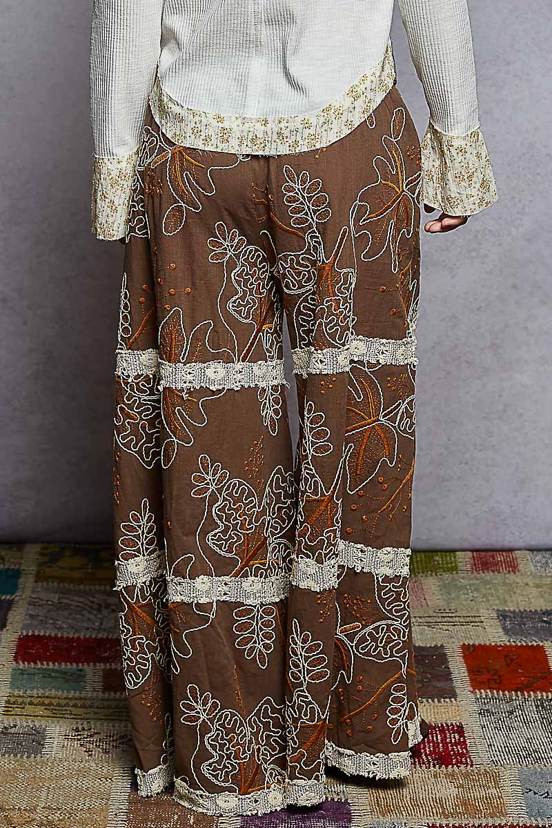 Brown pants with white floral embroidery on a patterned rug