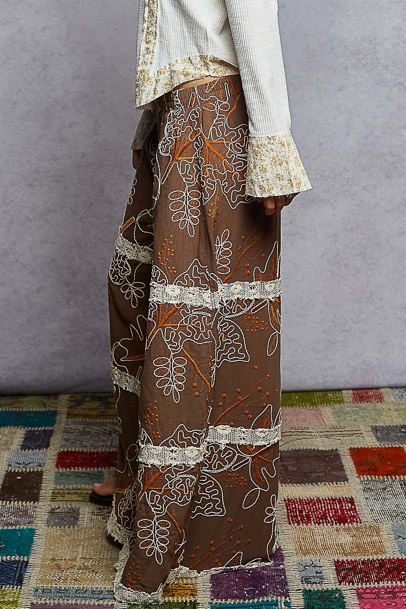 Brown patterned pants with white accents worn by a person on a colorful rug.