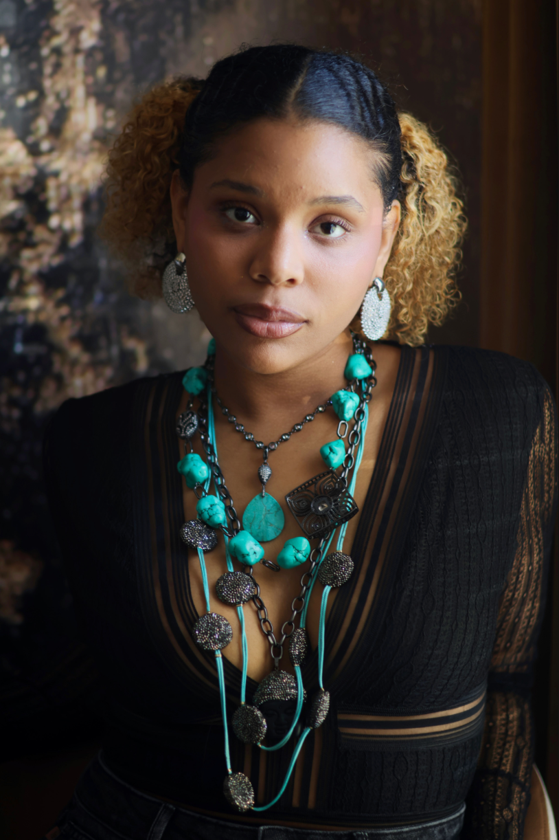 A woman wearing a turquoise and black stone necklace stack with matching earrings.