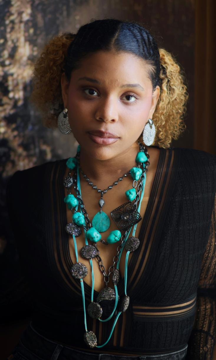 A woman wearing a turquoise and black stone necklace stack with matching earrings.