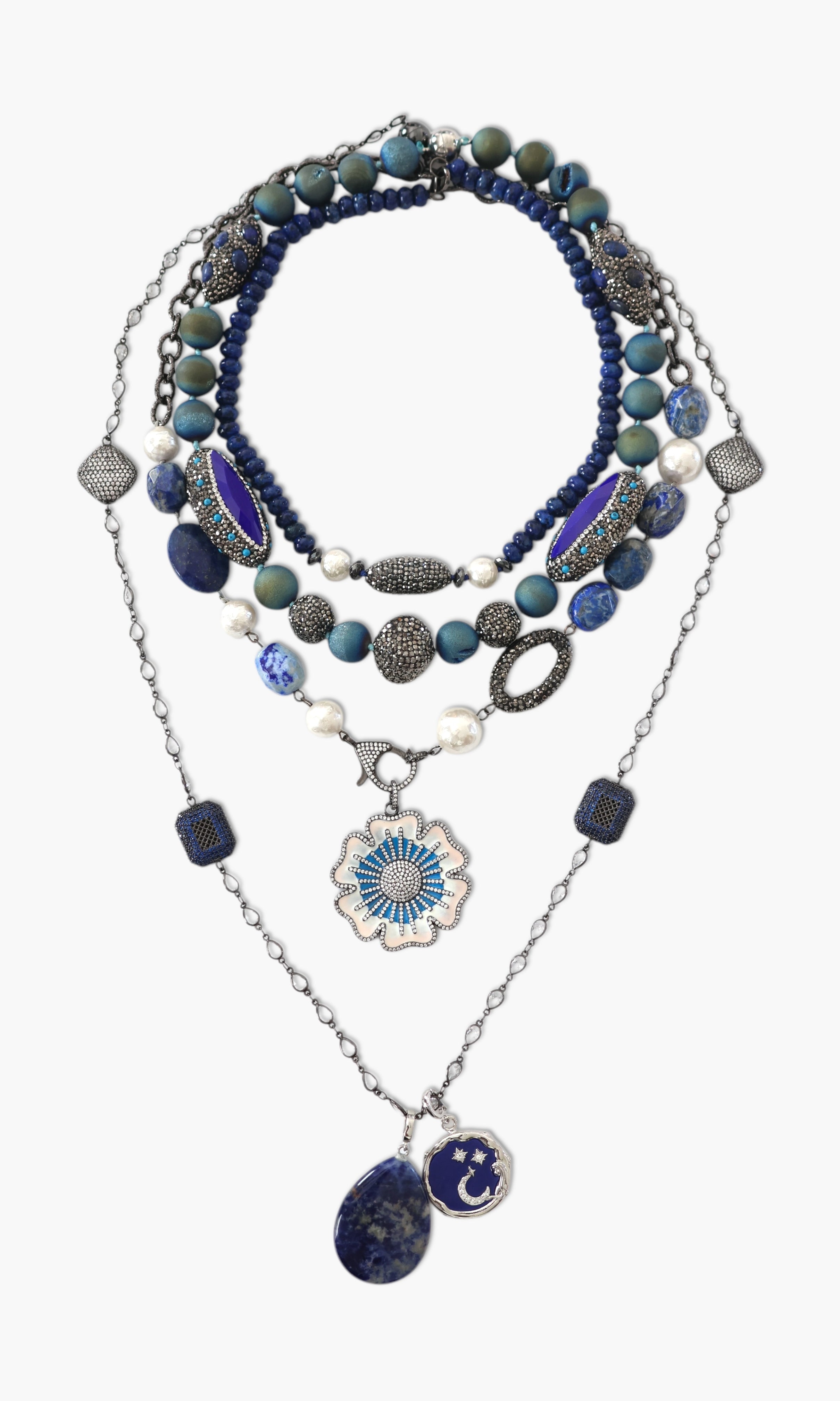 A person wearing a floral shirt and blue jeans, adorned with a stack of blue and gold necklaces featuring lapis lazuli and blue agate.