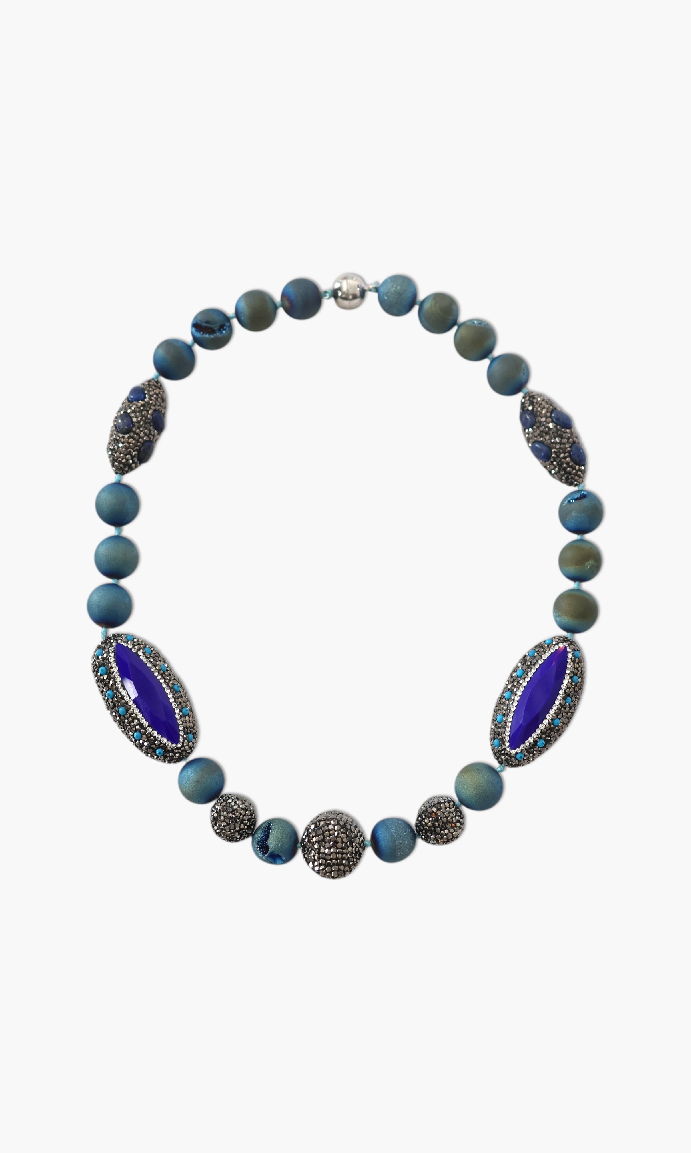 A person wearing a floral shirt and blue jeans, adorned with a stack of blue and gold necklaces featuring lapis lazuli and blue agate.