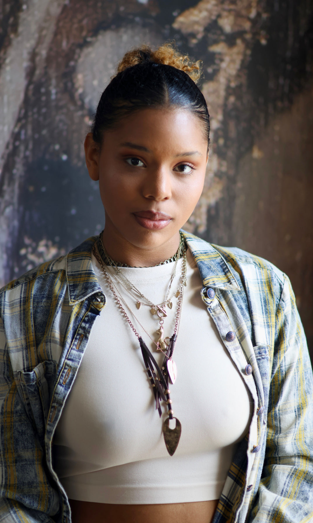A person wearing a brass necklace with a flowing design, featuring multiple layers and a prominent pendant.