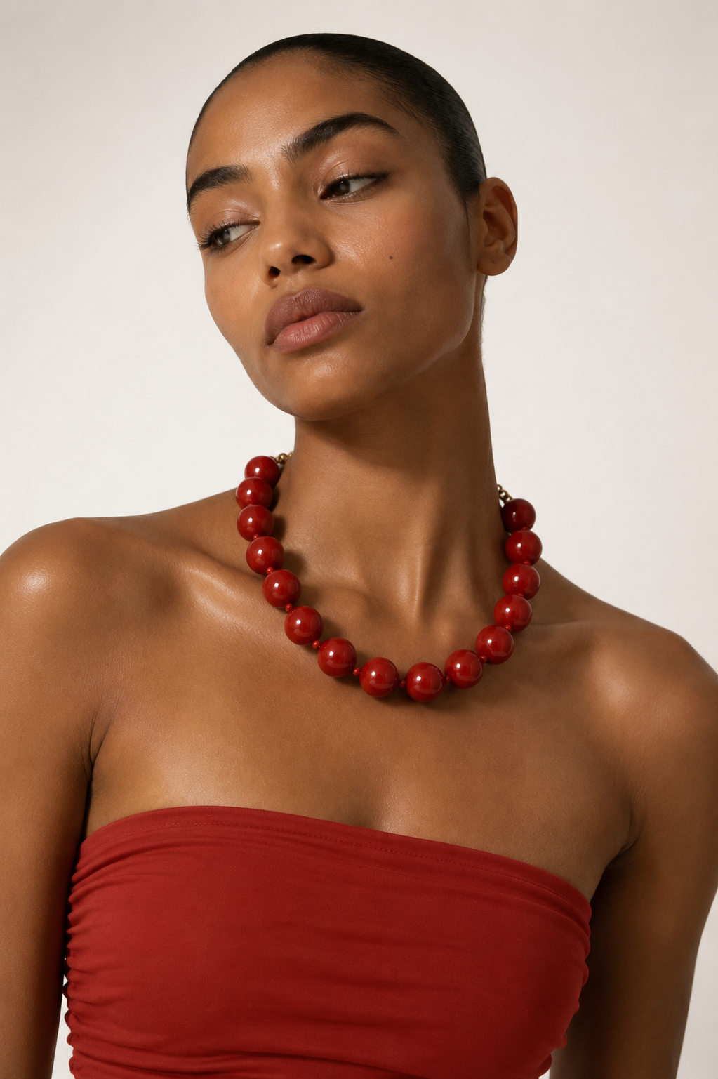 A close-up of a model wearing a chunky red beaded necklace and a matching red strapless top against a plain light background.