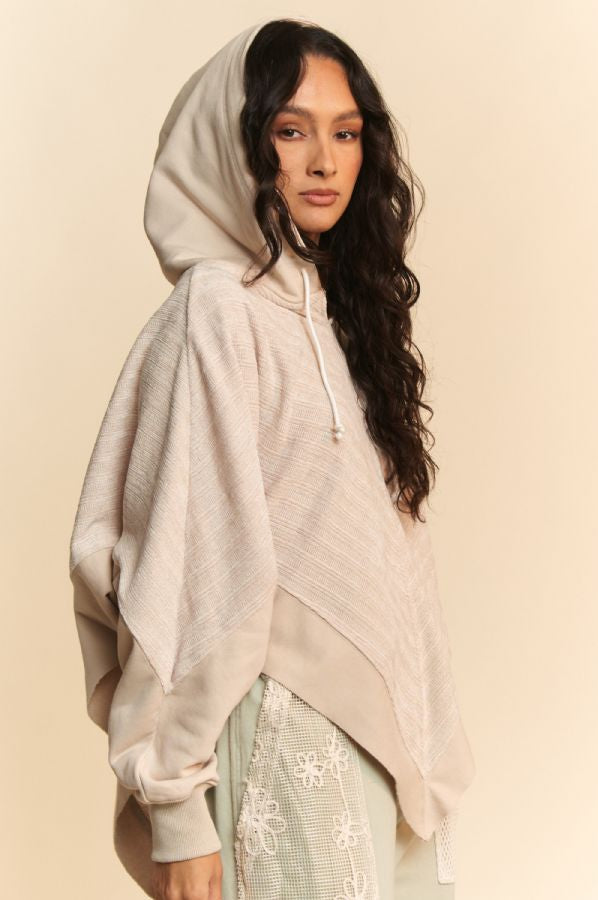 Woman wearing a beige hooded poncho over a light green outfit with floral patterns on a beige background