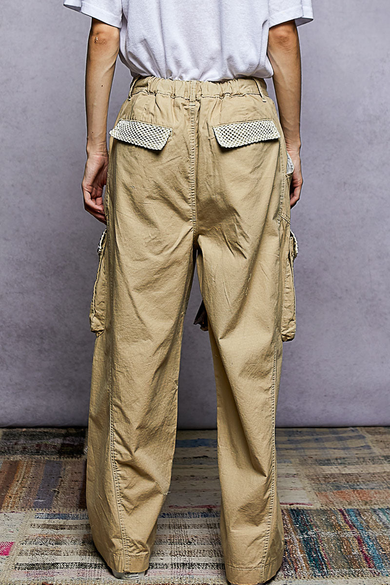 Person wearing beige cargo pants with decorative pockets against a plain background