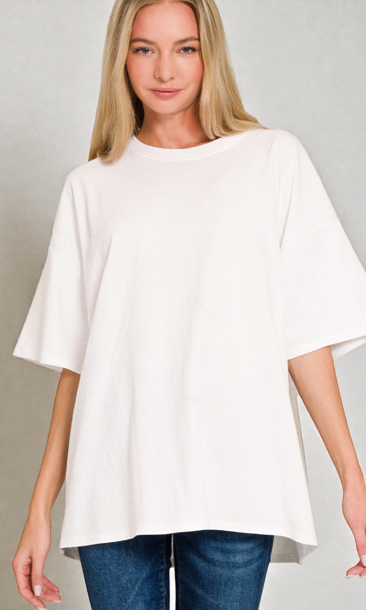 Woman wearing a white oversized top and blue jeans on a gray background