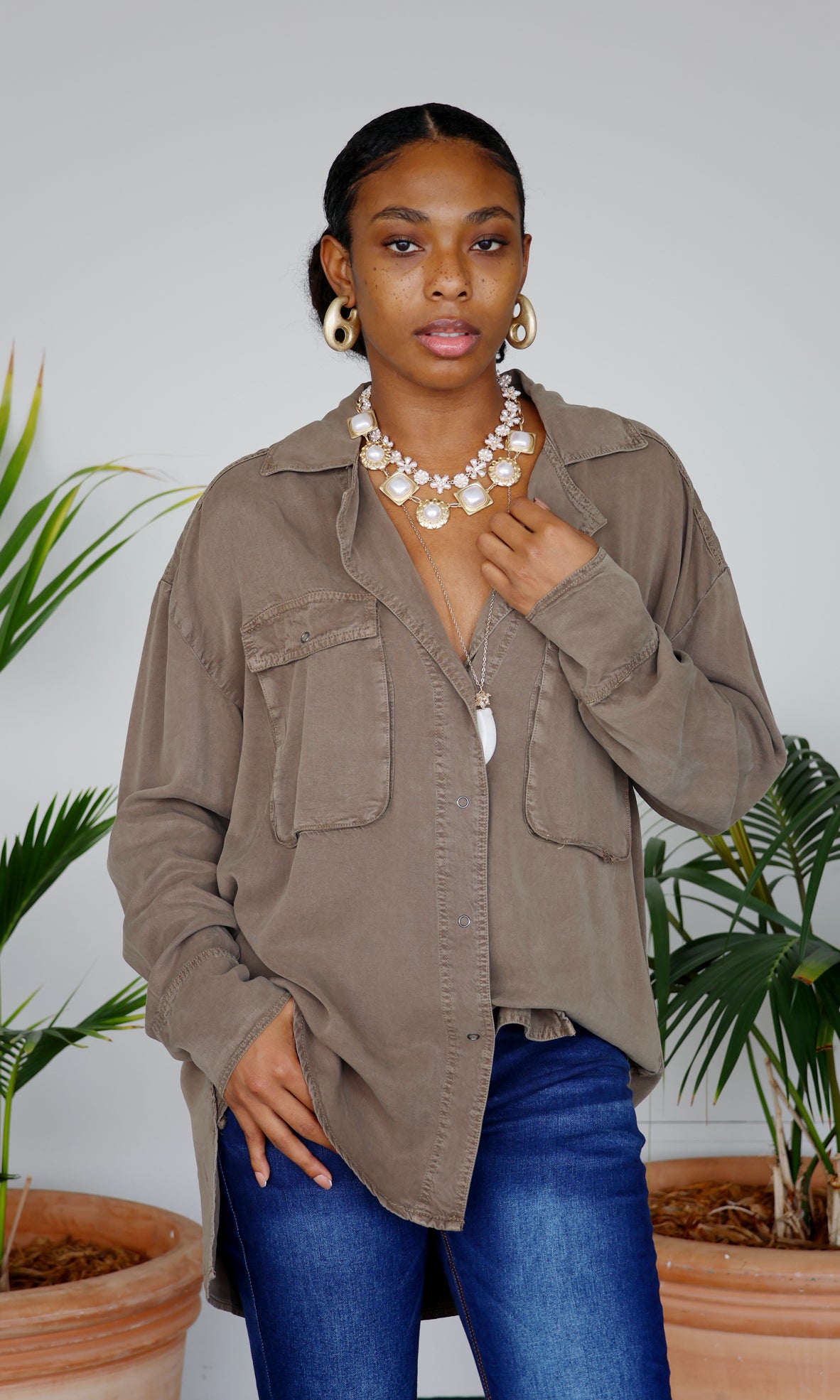 Woman wearing a brown jacket and blue jeans standing in front of plants
