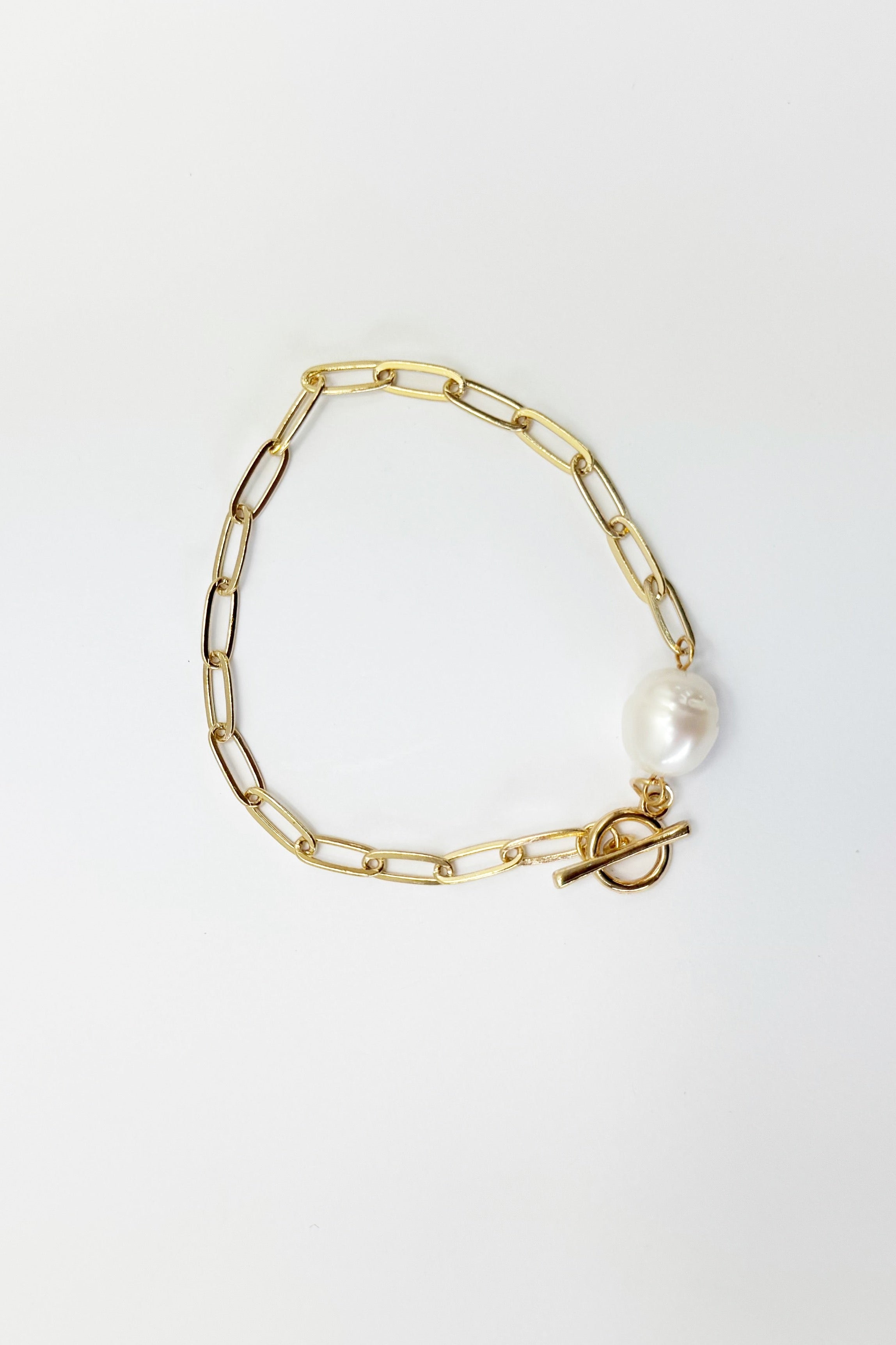 Gold chain bracelet with a pearl charm on a light gray background