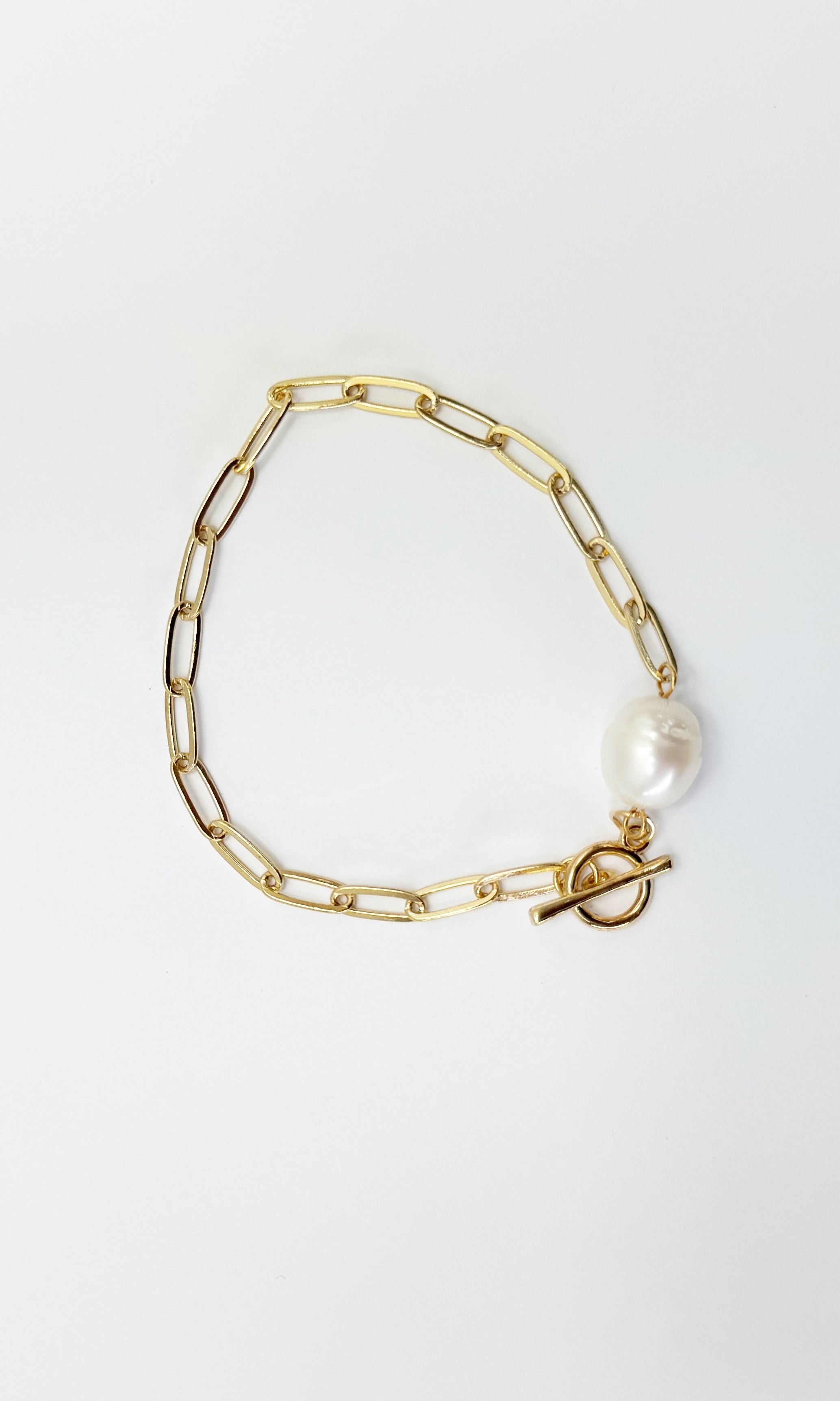 Gold chain bracelet with a pearl charm on a light gray background