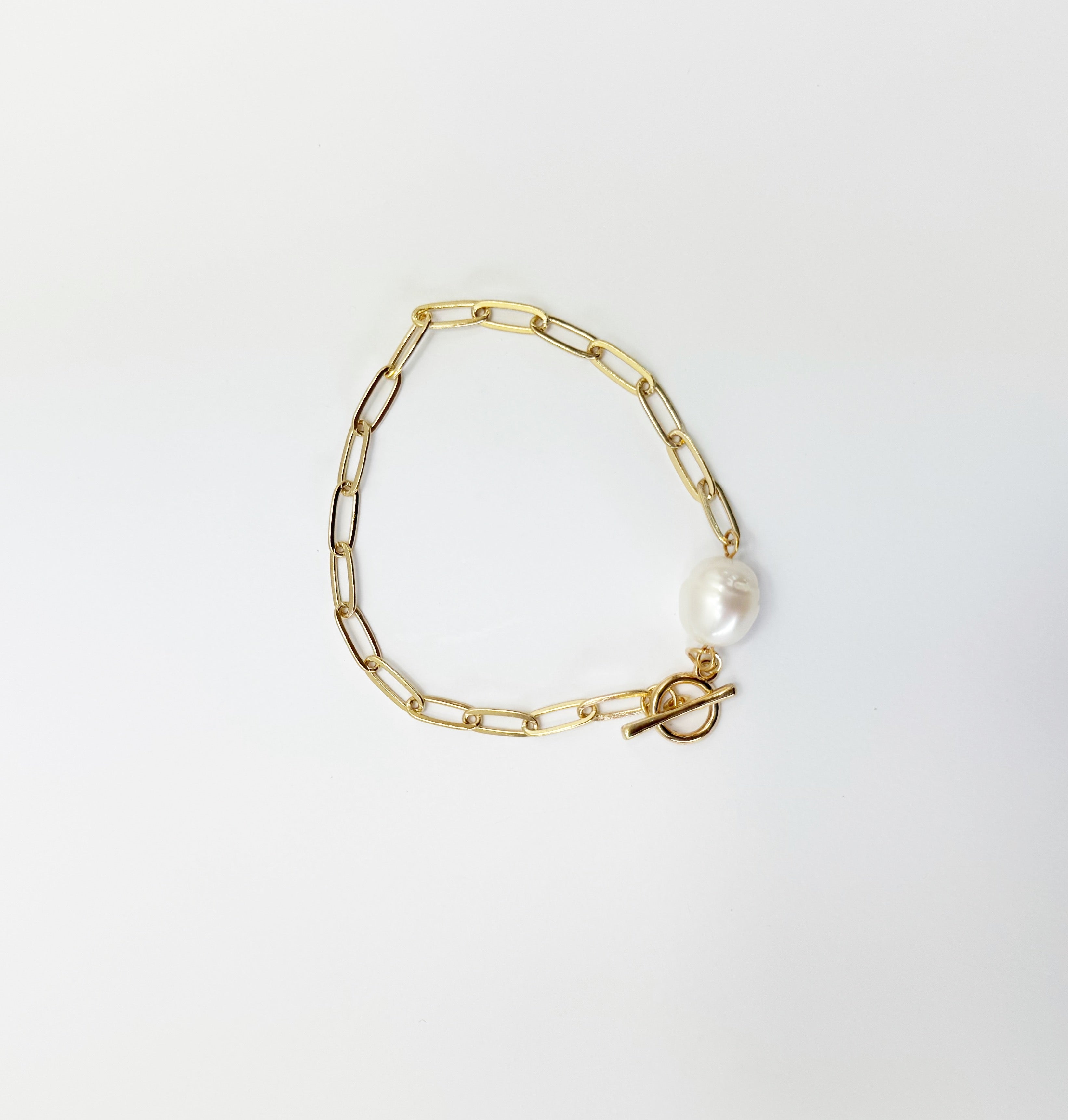 Gold chain bracelet with a pearl charm on a light gray background