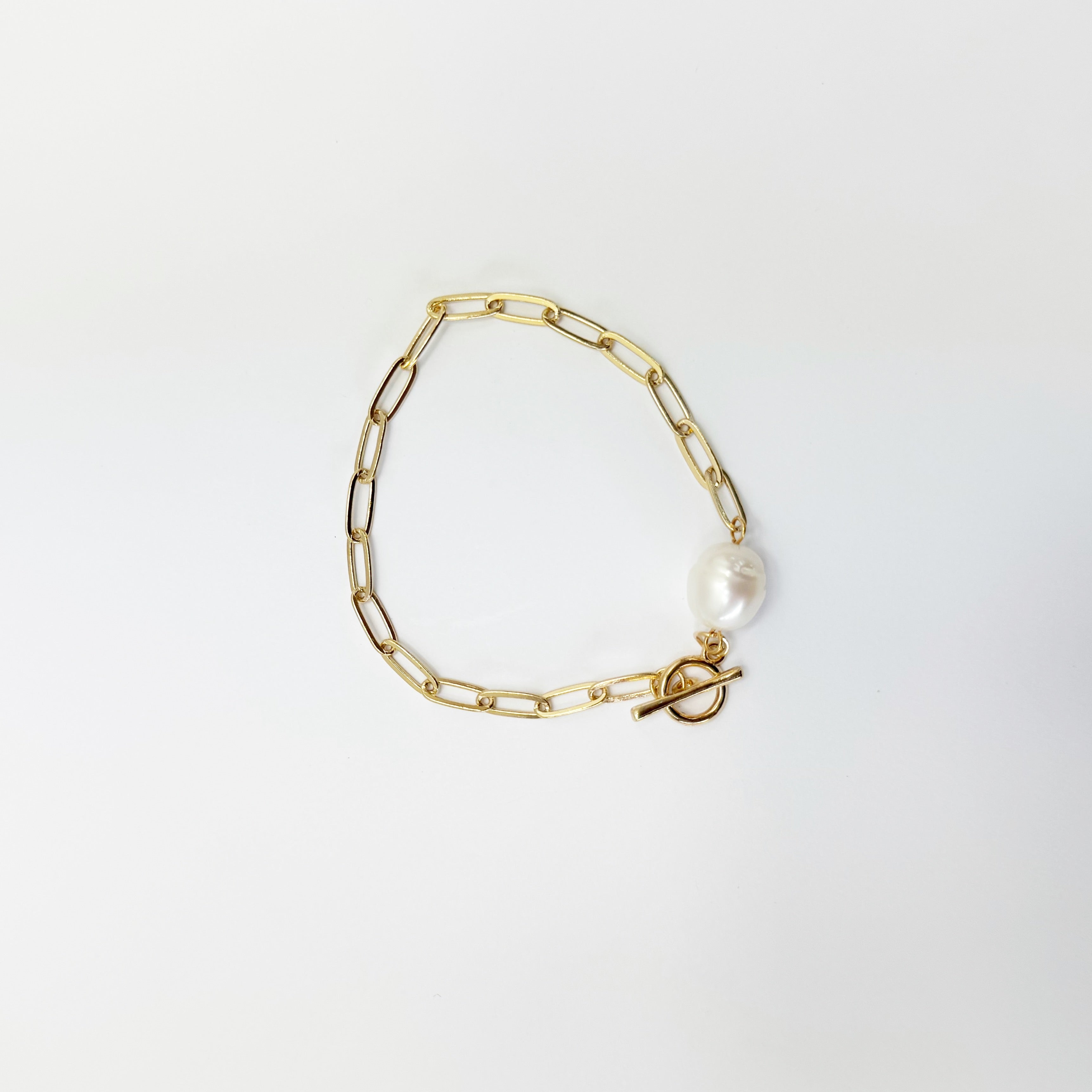 Gold chain bracelet with a pearl charm on a light gray background