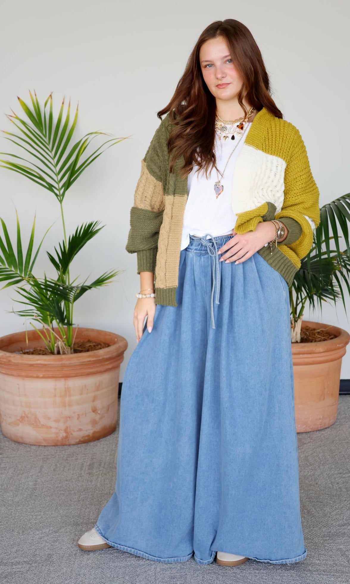Woman wearing a colorful cardigan and blue pants standing in front of potted plants.