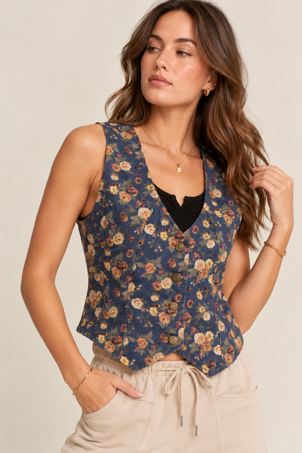 Navy floral denim vest with a V-neckline, button-front closure, fitted silhouette, and vintage-inspired multicolor floral print, layered over a black top and paired with cream drawstring pants.