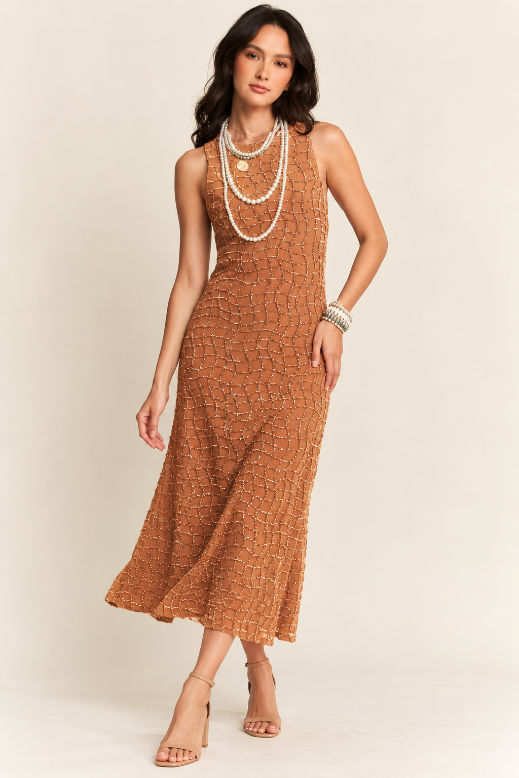Brown sleeveless midi dress with an intricate textured pattern, subtle shimmer, and a flowing A-line silhouette, styled with layered pearl necklaces, bracelets, and nude strappy heels.