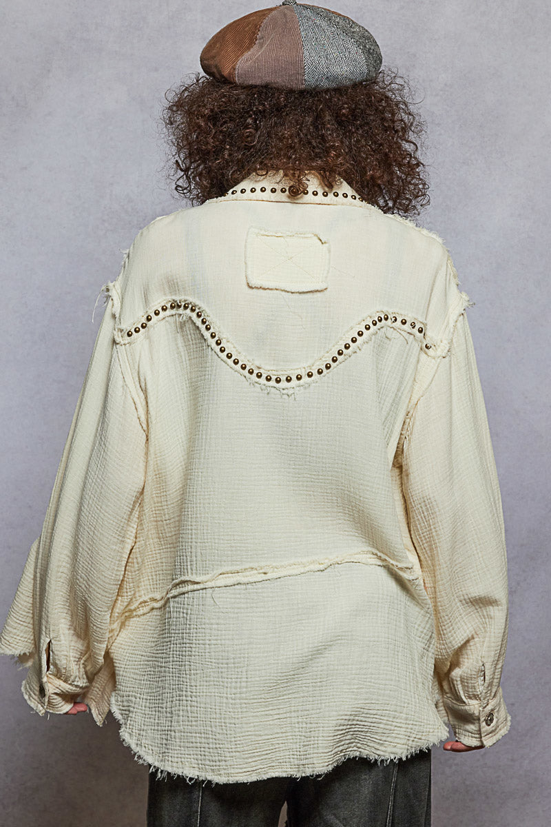 Person wearing a beige textured jacket with decorative elements on a gray background