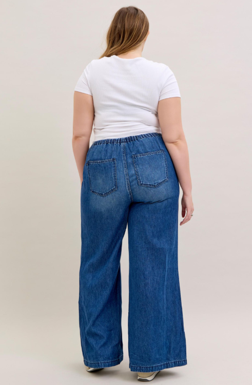 Person wearing blue wide-leg jeans and a white t-shirt on a beige background