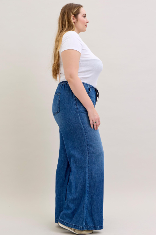 Woman wearing a white top and blue wide-leg jeans on a plain background
