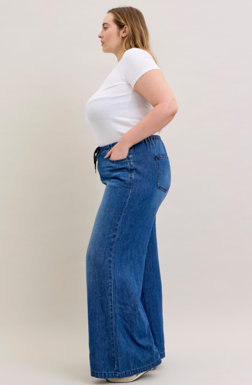 Woman wearing a white t-shirt and blue wide-leg jeans on a plain background