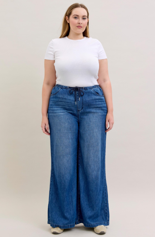 Woman wearing a white t-shirt and blue wide-leg jeans on a plain background