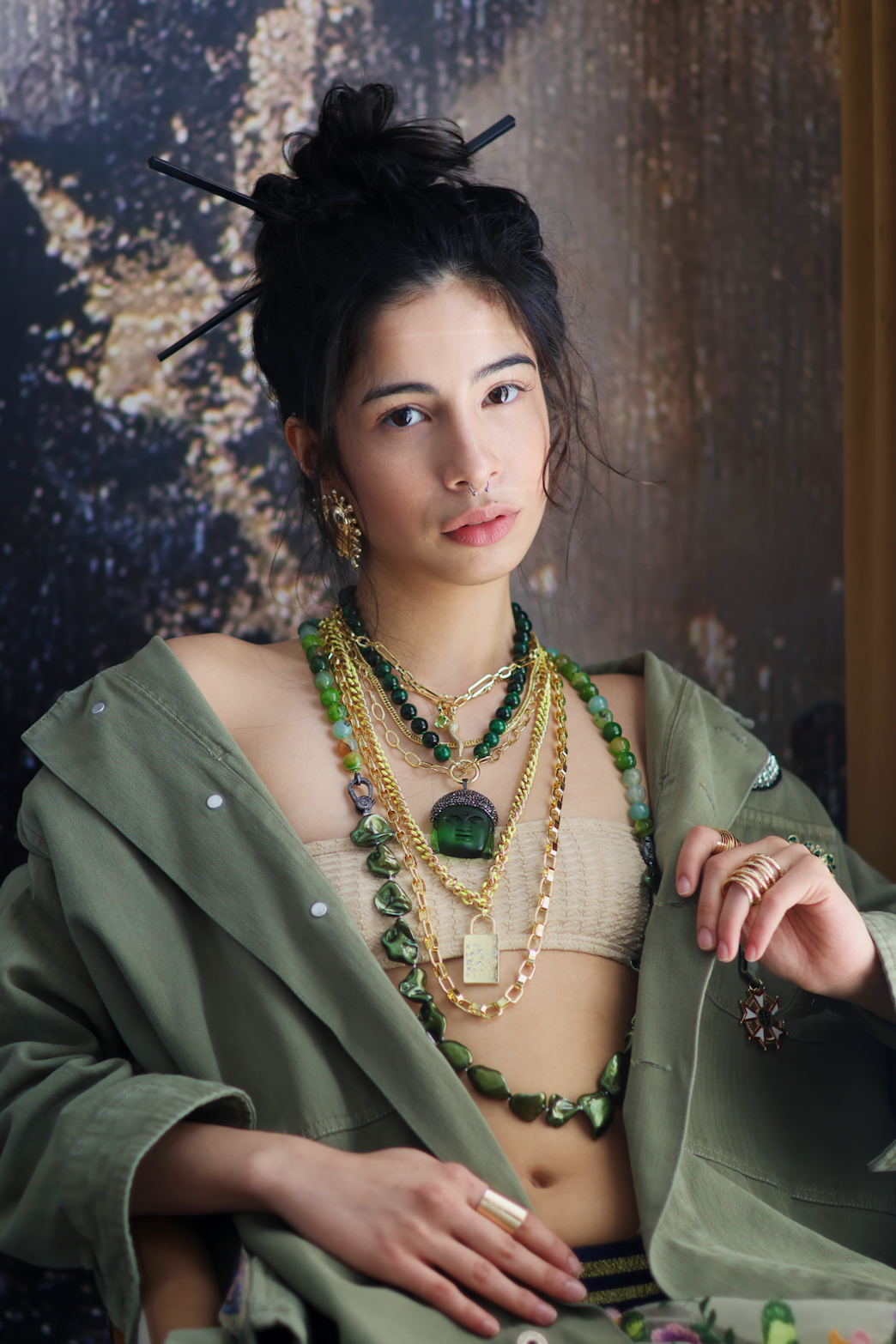 A person wearing multiple necklaces with green jade stones and gold accents. The necklaces are part of a stack, with some featuring intricate gold designs and others with plain green jade.