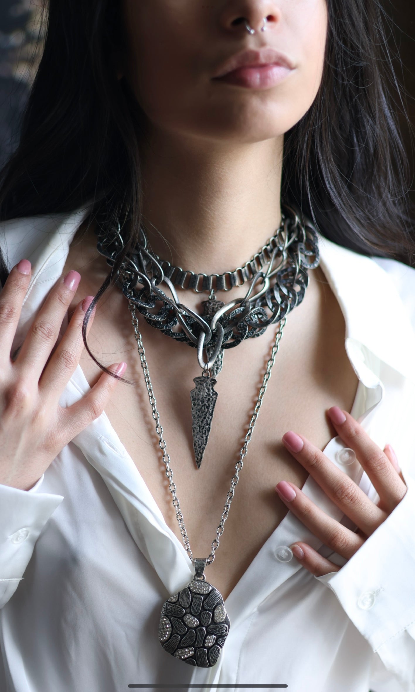 A person wearing a white shirt and a gunmetal-colored necklace with double arrow pendants.