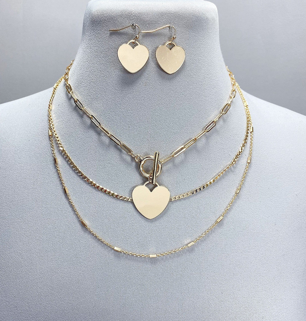 Gold heart-shaped necklace and earrings on a mannequin bust.