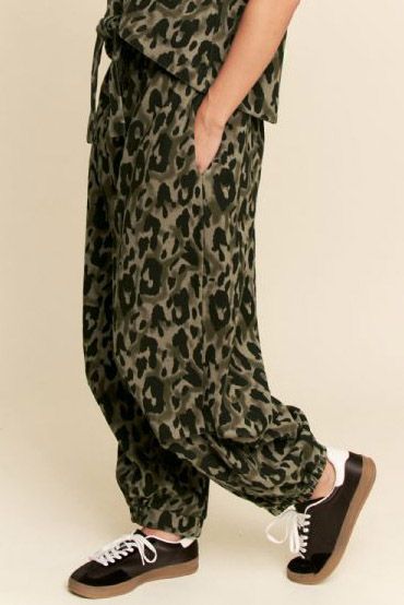 Person wearing leopard print pants with black sneakers on a beige background