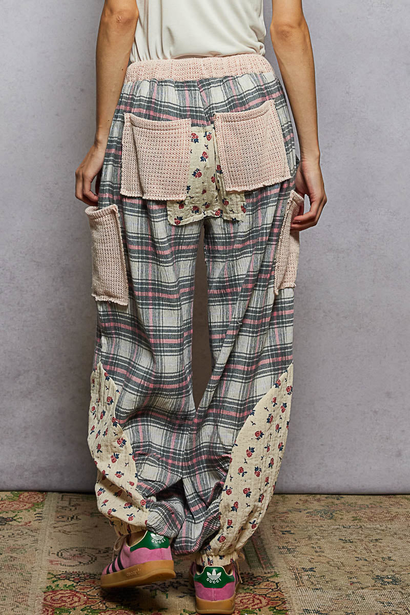 Plaid pants with floral patches worn by a person against a gray wall.
