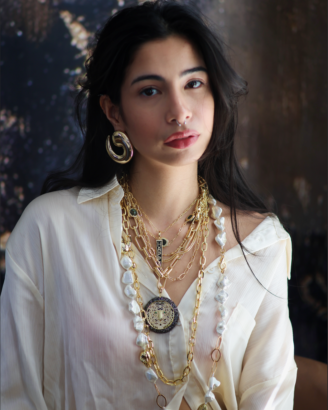 A woman wearing a white shirt and showcasing a stack of necklaces with gold accents and freshwater pearls.