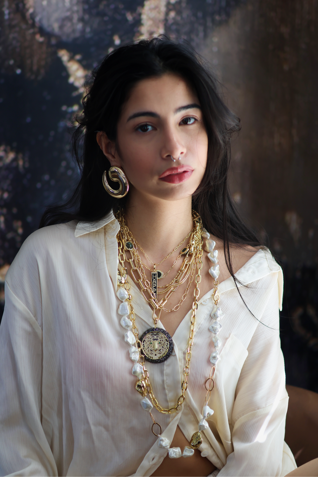 A woman wearing a white shirt and showcasing a stack of necklaces with gold accents and freshwater pearls.