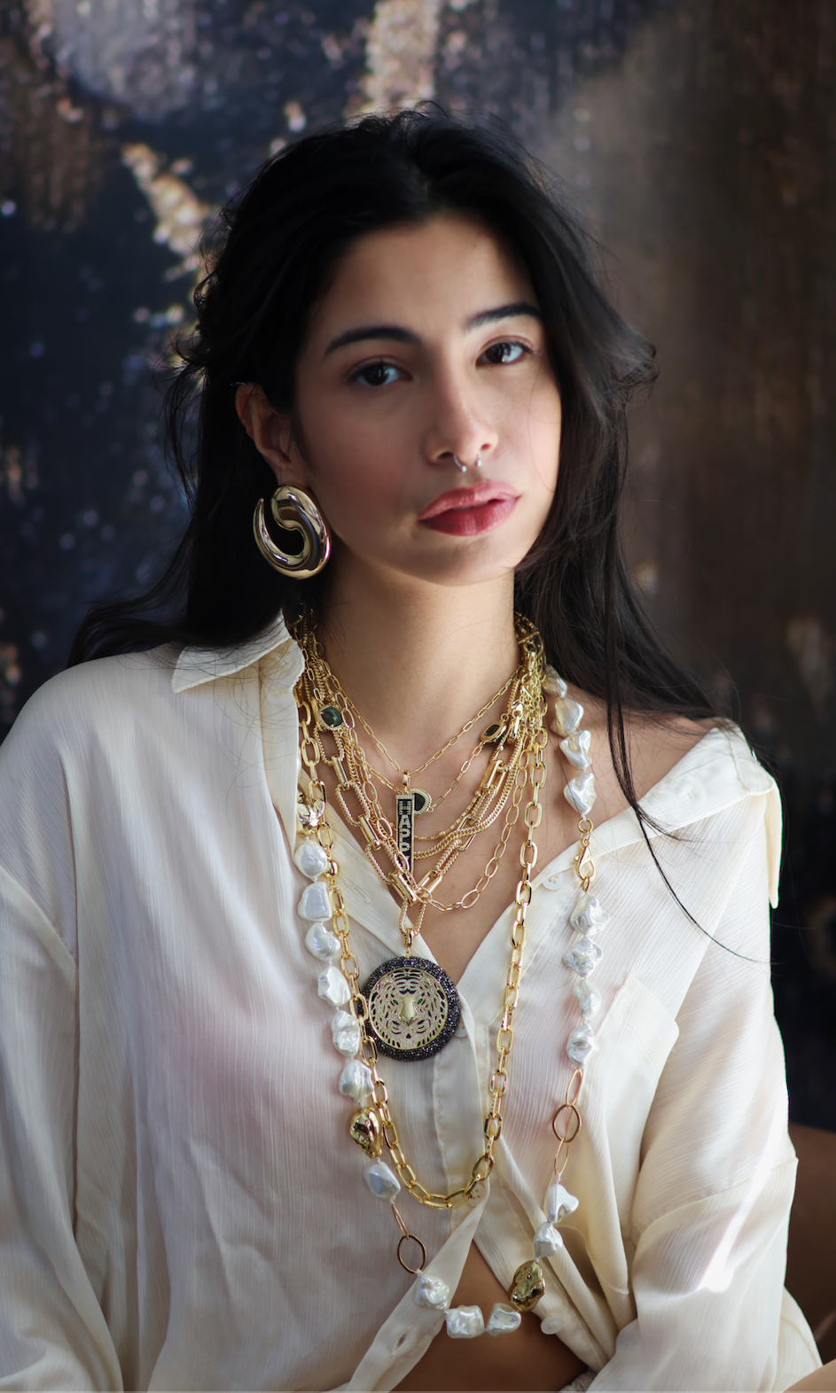 A woman wearing a white shirt and showcasing a stack of necklaces with gold accents and freshwater pearls.