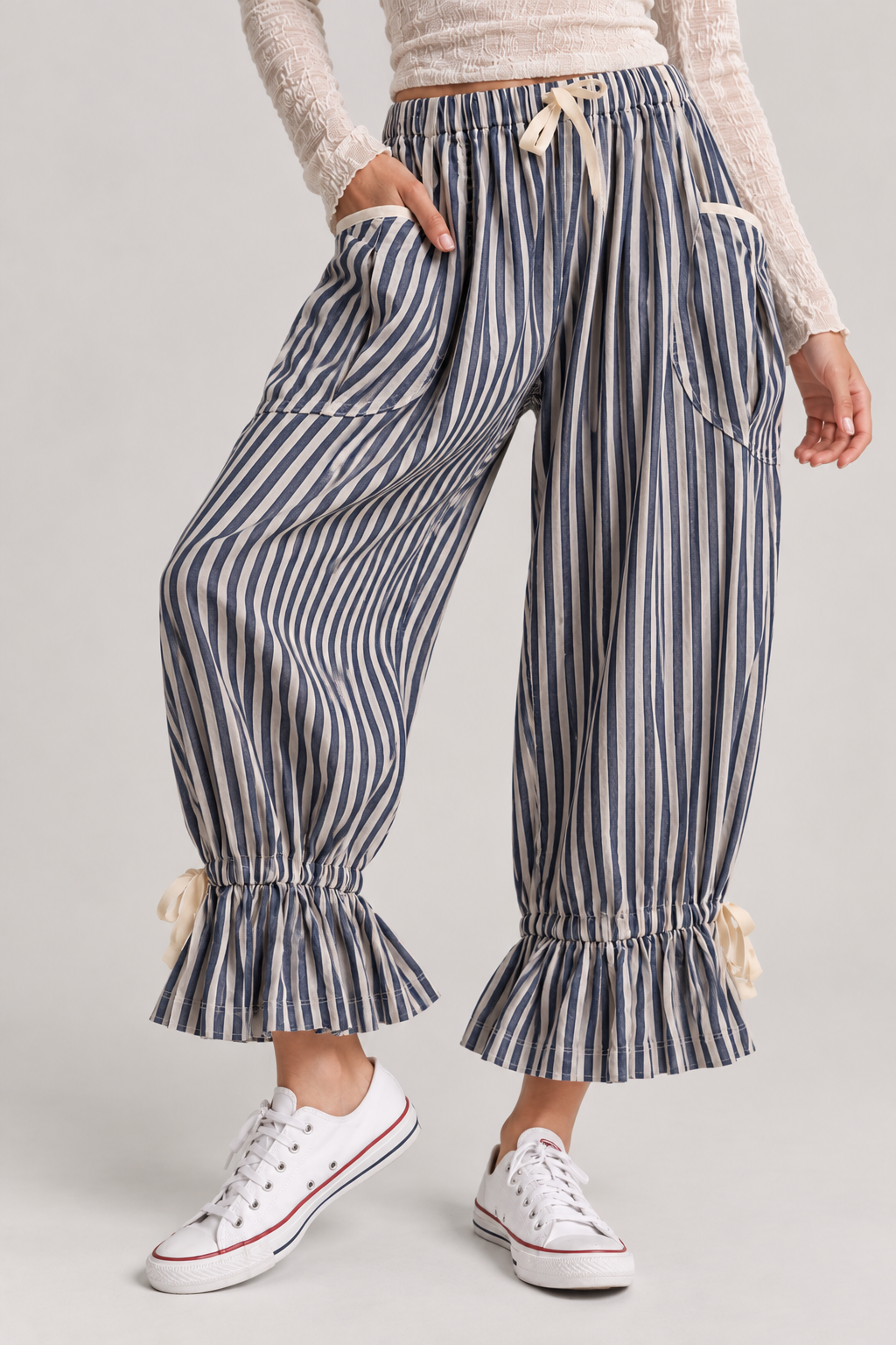 Navy and cream striped wide-leg pants with large patch pockets, drawstring waist, gathered ruffle cuffs, and ribbon accents, styled with a textured cream long-sleeve top and white sneakers.