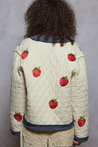 Person wearing a quilted jacket with strawberry patterns on a gray background
