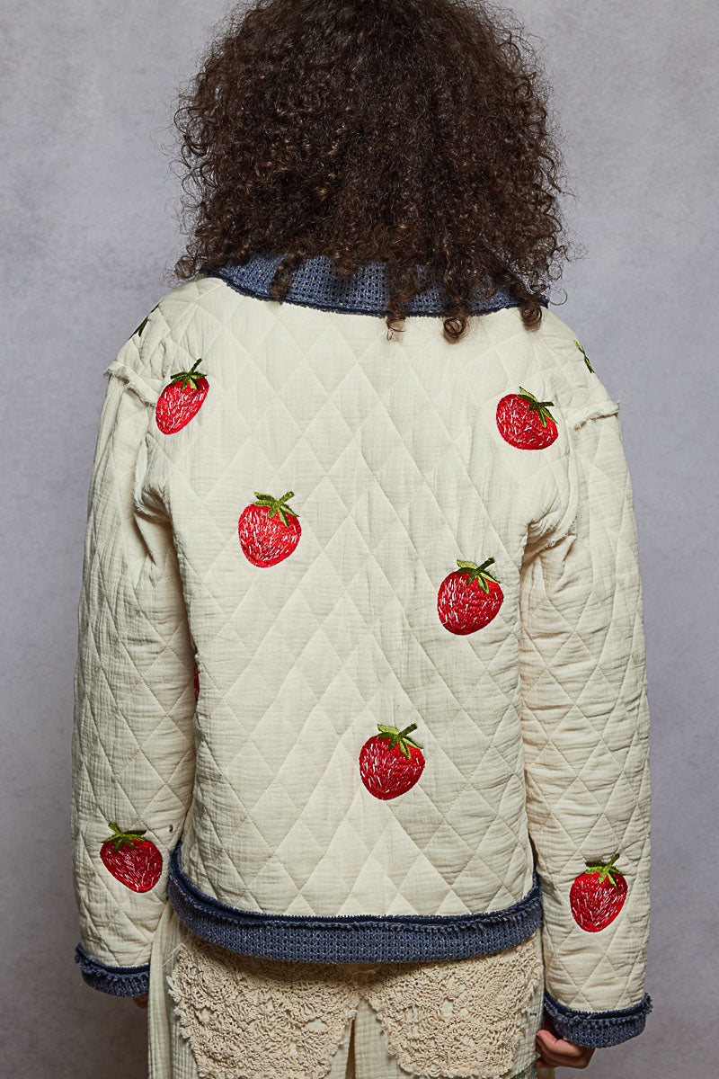 Person wearing a quilted jacket with strawberry patterns on a gray background