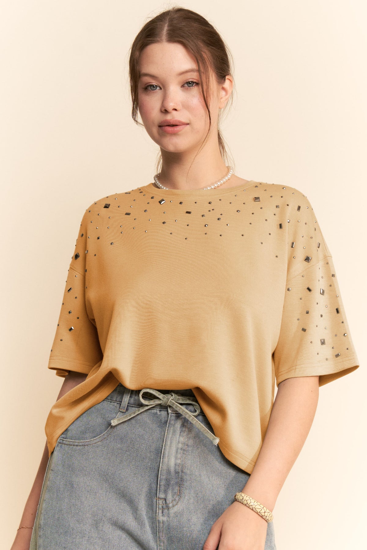 Woman wearing a mustard yellow top with black speckles and blue jeans on a beige background