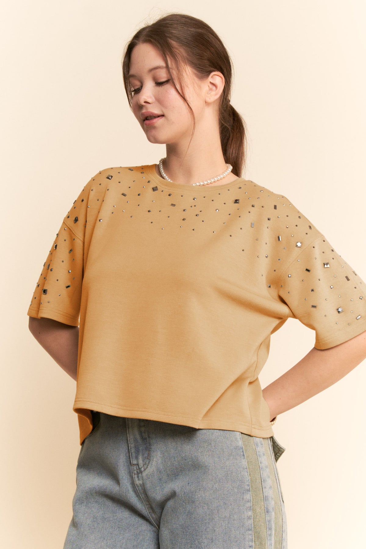 Woman wearing a beige t-shirt with rhinestone details on a beige background