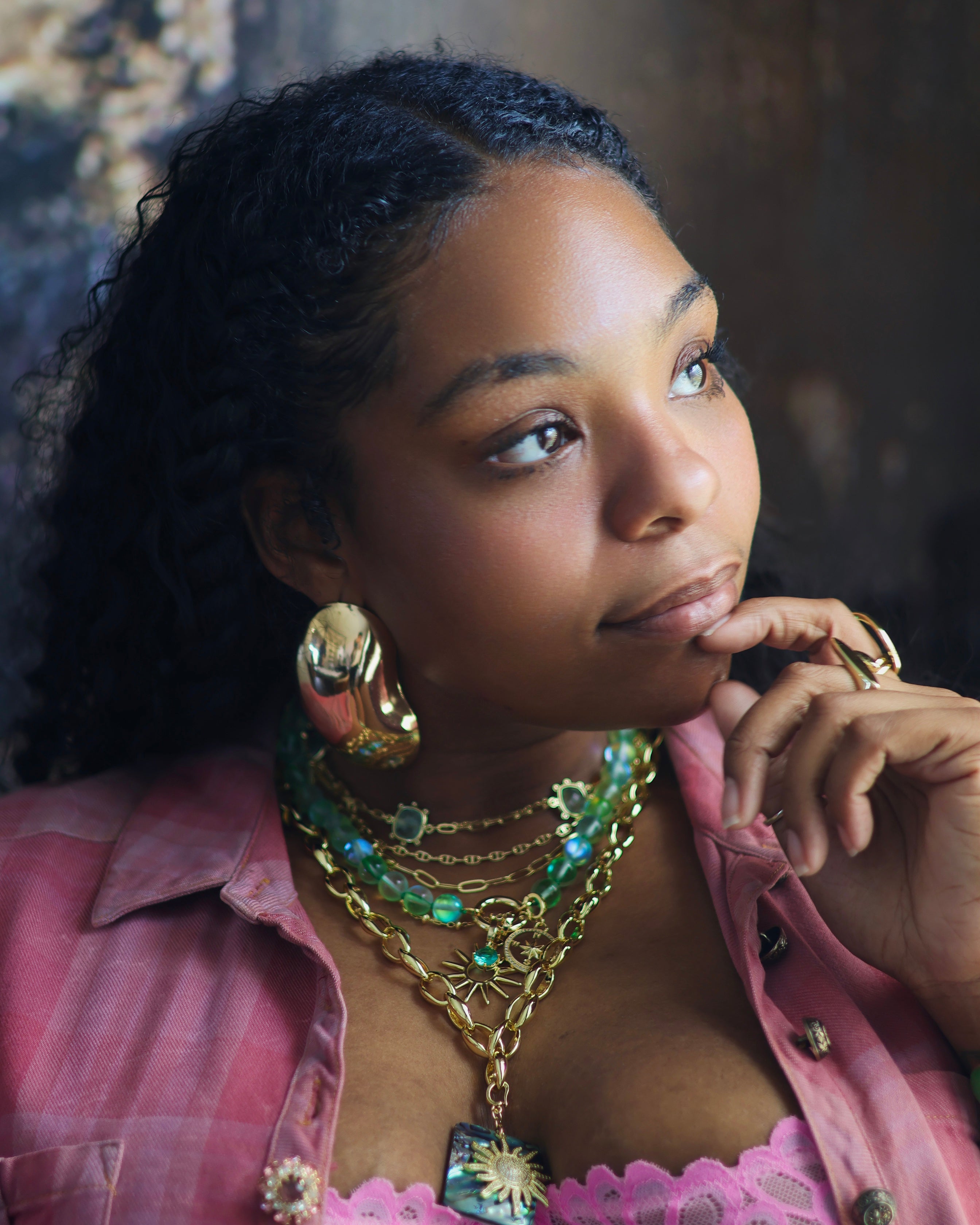 This image features a collection of vibrant and ornate jewelry, presented on a model who adds a touch of elegance. The jewelry set includes multiple necklaces with intricate designs, featuring a mix of gold and green hues, along with matching earrings and a bracelet.