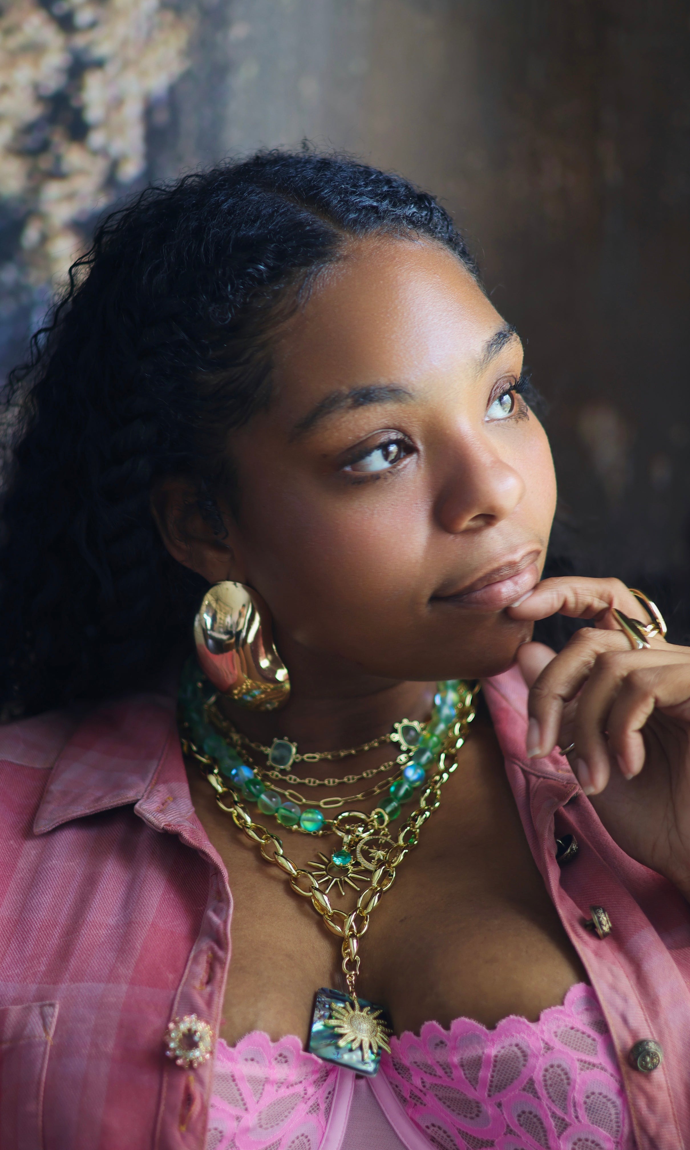 This image features a collection of vibrant and ornate jewelry, presented on a model who adds a touch of elegance. The jewelry set includes multiple necklaces with intricate designs, featuring a mix of gold and green hues, along with matching earrings and a bracelet.