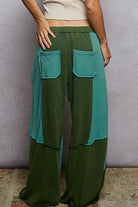 Green and teal layered pants worn by a person against a plain background