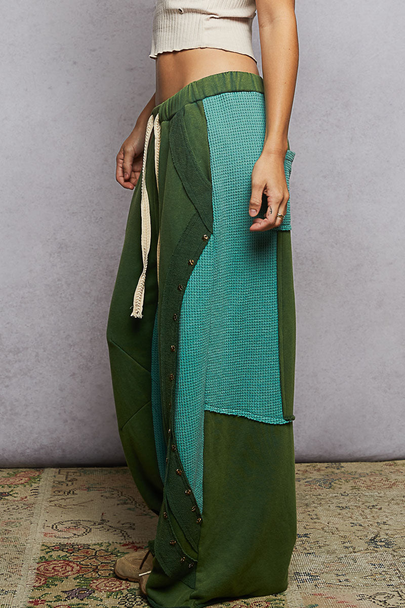Green and teal patterned pants worn by a person against a plain background