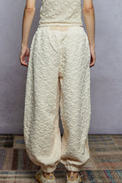 Person wearing textured beige pants and top against a plain background
