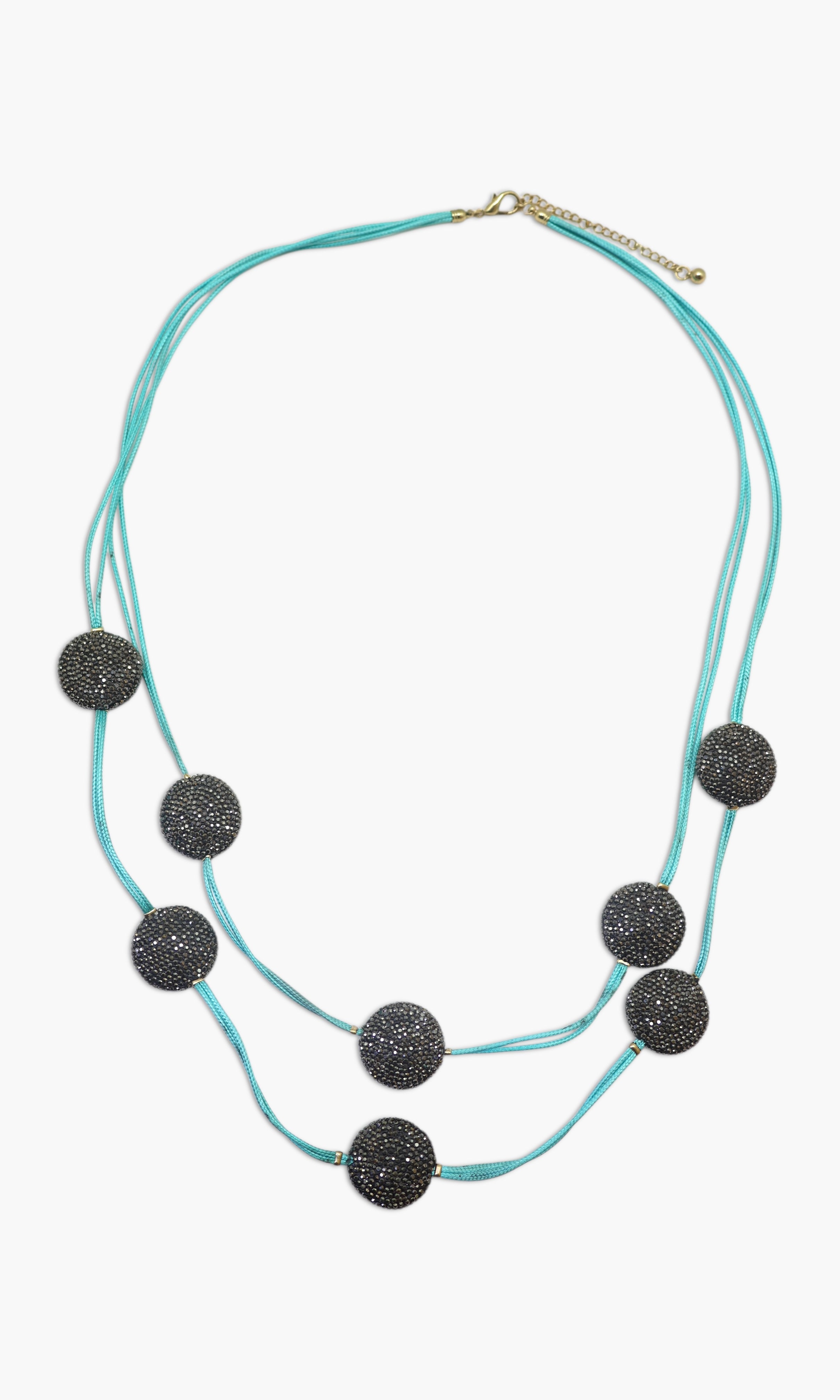A woman wearing a turquoise and black stone necklace stack with matching earrings.