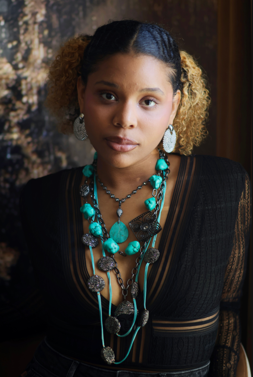 A woman wearing a turquoise and black stone necklace stack with matching earrings.
